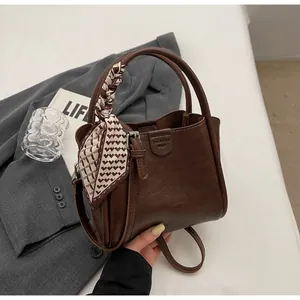 Détail d'un sac seau marron foncé avec foulard à carreaux et logo gaufré élégant