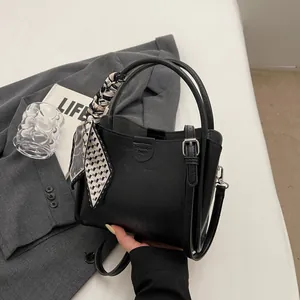 Sac seau noir élégant avec foulard en soie sur la poignée posé sur une veste grise