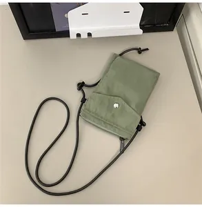 Detalle de mini bolso bandolera de nailon verde salvia con botón a presión y correa ajustable