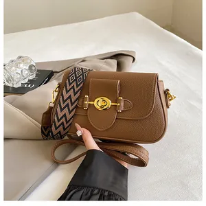 Détail du sac marron avec motif litchi, large bandoulière tissée et fermoir doré chic