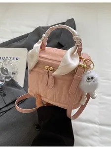 Pink patent leather crossbody bag with silk-wrapped handle and furry charm on grey suit