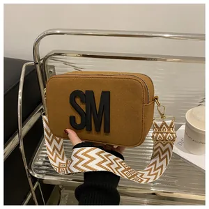 Detail of tan suede camera bag with bold SM letter and geometric wide woven strap
