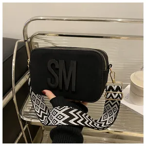 Detail of black suede camera bag with SM logo and geometric woven wide strap