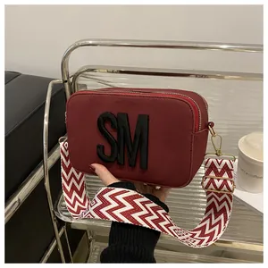 Detail of red suede camera bag with SM logo and geometric wide shoulder strap