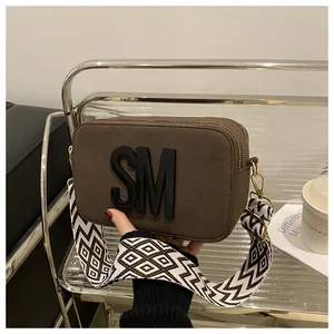 Detail of a brown camera bag with black SM logo and wide geometric shoulder strap