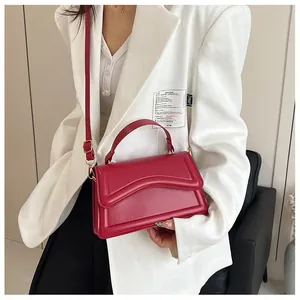 Detail of red leather crossbody bag with wavy flap shown on a white blazer outfit