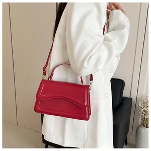 Detail of bright red wave-flap crossbody bag with top handle and adjustable strap