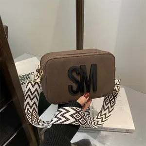 Dark brown camera bag with geometric wide strap and 3D letters for a modern style