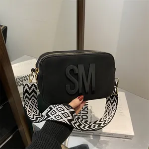 Black camera crossbody bag with bold SM logo and wide geometric diamond strap