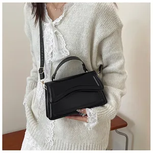 Detail of a black minimalist leather crossbody bag with gold hardware and top handle