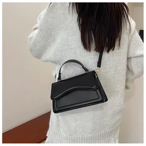 Close-up of black crossbody bag with curved flap detail and gold buckle on a model