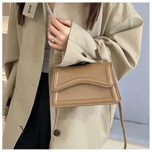 Detail of tan leather crossbody bag with wave edge flap shown on model with khaki trench coat