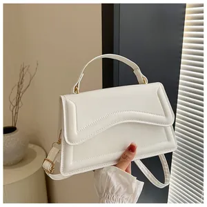 Detail of white quilted crossbody bag featuring gold hardware and a top handle