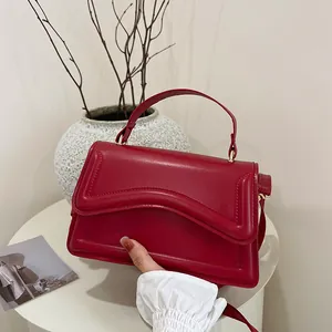 Chic red faux leather crossbody bag with wavy flap design on a white stylist table