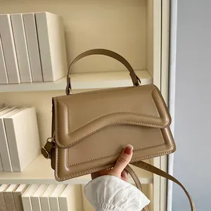 Elegant khaki leather crossbody bag with wave-edge flap and top handle held by hand