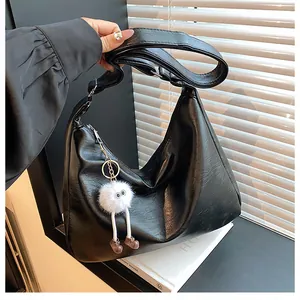 Detail of black PU leather hobo bag with a cute plush doll charm and adjustable strap