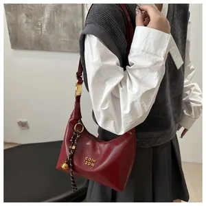 Detail der burgunderfarbenen Hobo-Tasche mit Goldbeschlägen und Anhänger am Schultergurt