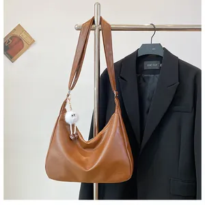 Detail view of brown matte leather shoulder bag with a white plush charm on a hanger
