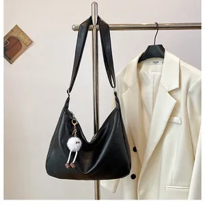 Detailed view of a black glossy faux leather hobo bag with a white fuzzy monster charm