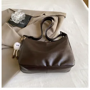 Detail of dark brown leather hobo bag with pebble texture and white plush charm