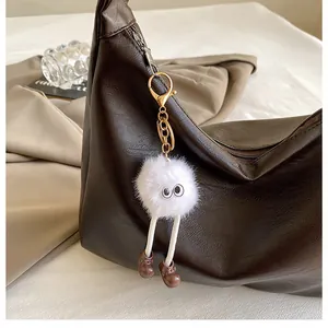 Detail of creative white fluffy plush charm with large eyes on a brown leather handbag