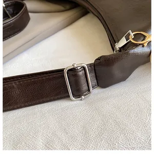 Detail of adjustable silver buckle on dark brown textured leather shoulder bag strap