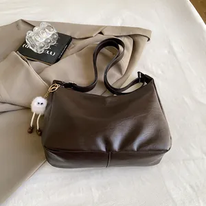 Detail of dark brown faux leather tote with creative white fur ball charm and wide strap