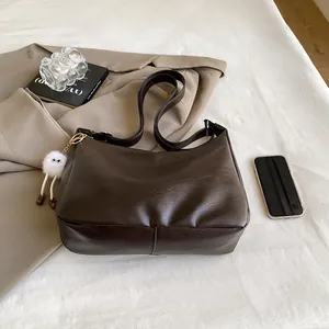 Detail of a large dark brown faux leather shoulder bag with a plush charm on neutral fabric