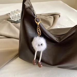 Detail of a white plush monster keychain with big eyes on a brown leather handbag