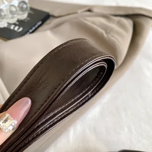 Close-up of brown litchi grain leather strap with precise stitching on a beige bag