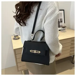 Sac noir à motif litchi avec fermoir doré porté sur un pull en maille crème