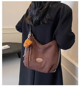 Détail d'un sac hobo en daim marron avec breloque chiot porté sur un manteau noir