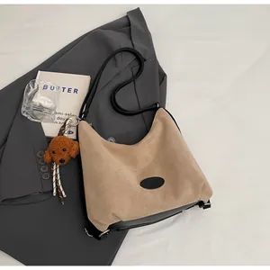 Détail du sac bandoulière en daim kaki avec base en cuir noir et breloque en peluche