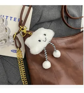 Detail of a white plush cloud charm with an embroidered smile and chain on a brown tote