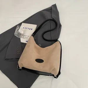 Sac fourre-tout vintage en daim beige avec bordure noire posé sur une veste grise
