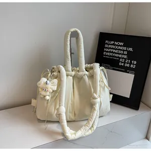 Detalle del bolso beige con cordón y colgante de felpa sobre superficie de mármol