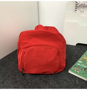 Détail d'un sac à dos en nylon rouge avec poche zippée sur un tissu texturé résistant