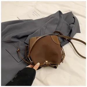 Détail du sac seau vintage marron avec texture mate et cordons sur un blazer gris