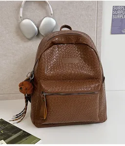 Detail eines braunen Rucksacks mit Webstruktur, Plüschbär-Anhänger und Ledergriff
