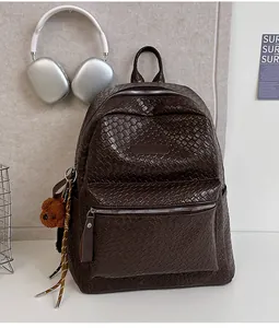 Detail eines dunkelbraunen Rucksacks mit Webstruktur, Bärenanhänger und Kopfhörern