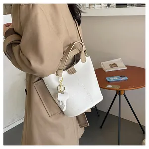 Detailansicht der weißen Eimer-Tasche aus Litschileder mit braunem Griff und Elefantenanhänger