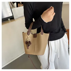 Detail der khakifarbenen Beuteltasche mit Lederstruktur und floralem Anhänger-Accessoire