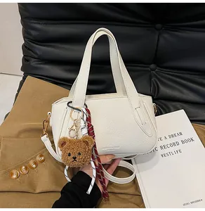 Detail of white lychee leather texture with cute teddy bear and woven charms on handbag