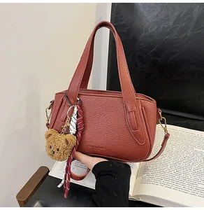 Close-up of brick red lychee textured handbag with plush bear charm and woven strap