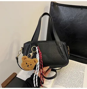 Detail of black lychee grain leather handbag with gold hardware and plush bear charm