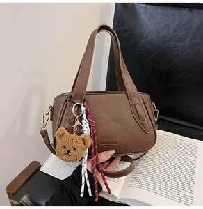 Detail of a dark brown lychee-textured leather handbag with a plush bear charm on a black chair