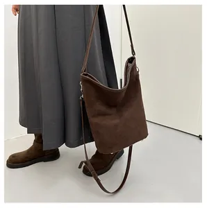Vue latérale du sac seau en daim marron foncé porté par un mannequin en tenue chic