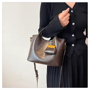 Dettaglio borsa a secchiello in pelle marrone scuro con mini ciondolo e hardware dorato