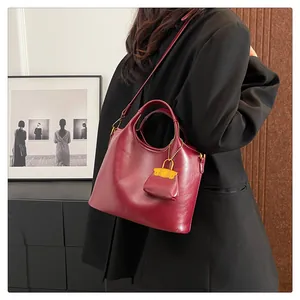 Dettaglio della borsa tote bordeaux con ciondolo giallo su outfit con blazer nero