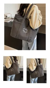 Dettaglio borsa tote in tela grigio scuro con scritte artistiche e ampia tracolla